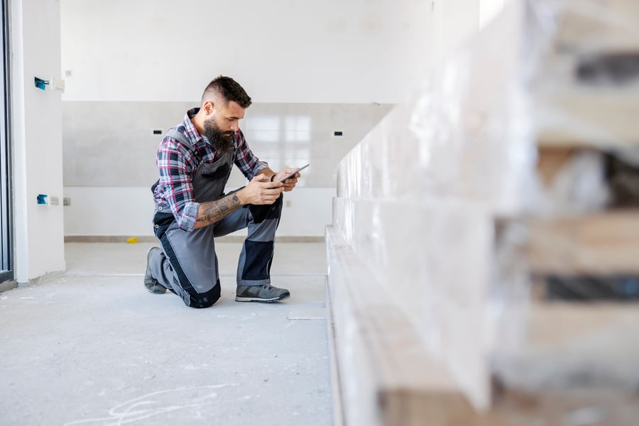 A man in overalls is kneeling inside the new building and checking on materials on his tablet